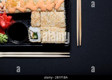 Sushi-Rollen im Set, die mit Holzstäbchen auf schwarzem Tuch weggenommen werden können. Stockfoto