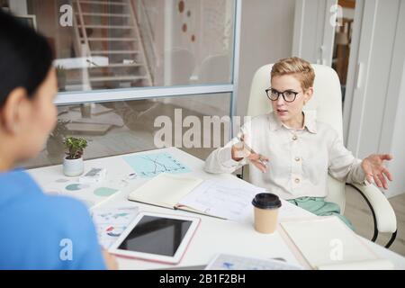 Porträt der modernen kurzhaarigen Frau, die mit Kollegen oder Partnern über einen Tisch im Büro streitet, Platz für Kopien Stockfoto