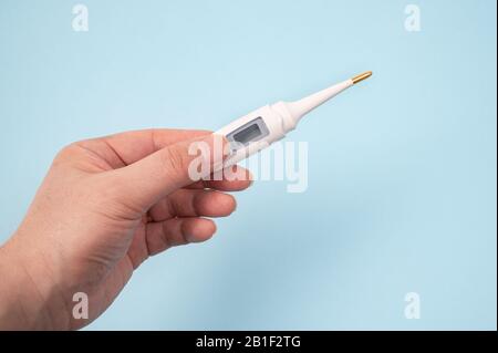 Eine männliche Hand, die ein Digitalthermometer auf blauem Hintergrund in der Hand hält Stockfoto