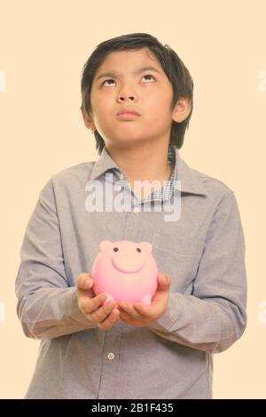 Studio shot von cute Japanese boy Holding piggy Bank beim Denken Stockfoto