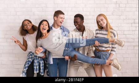 Freudige multiethnische Gruppe von Teenagern, die asiatische Mädchen hochheben Stockfoto