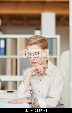 Porträt einer pensive tätowierten Geschäftsfrau, die im Büro am Schreibtisch arbeitet Stockfoto