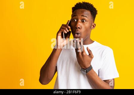 Staunender afrikanischer Kerl, der überraschend mit Gesicht telefoniert Stockfoto