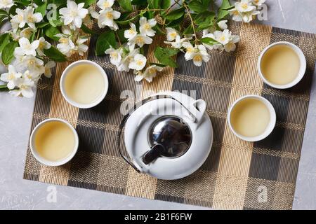 Asiatischer Teeset aus weißem Porzellan mit grünem Tee und Jasmin auf Bambusnapkin, Draufsicht. Stockfoto