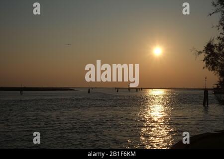 Ein venetianischer Sonnenuntergang von der Insel Burano, ein Band aus Rosengoldhimmel, Kanalmarkierungen und gewelltem Wasser, das die Sonne über die Lagune, Venedig, Italien reflektierte Stockfoto