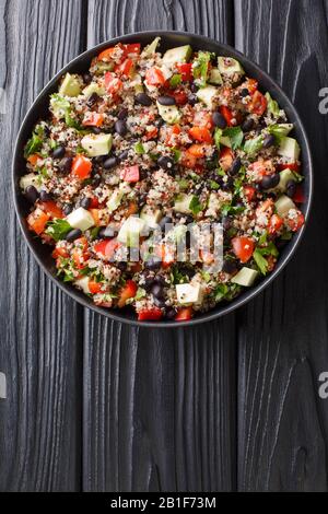 Chinoa im mexikanischen Stil mit frischen Avocado, Paprika, Tomaten und schwarzen Bohnen in einem Teller auf einem Tisch. Vertikale Draufsicht von oben Stockfoto