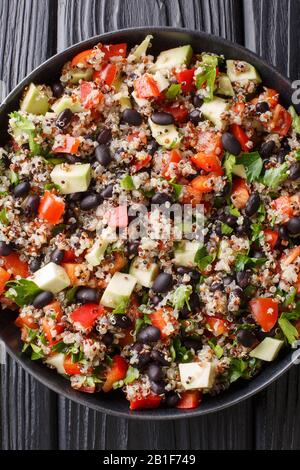 Mexikanischer Chinoa-, Avocado-, Paprika-, Tomaten- und Schwarzbohnensalat in einem Teller auf dem Tisch. Vertikale Draufsicht von oben Stockfoto