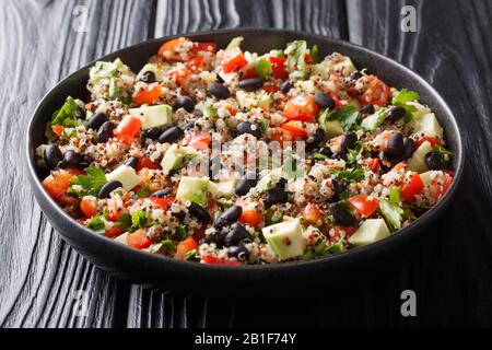 Gesund gefärbte Quinoa, Avocado, Pfeffer, Tomaten und schwarze Bohnen liegen in einem Teller auf dem Tisch. Horizontal Stockfoto