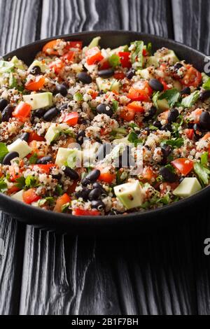 Gekochtes Quinoa mit frischen Avocado, Paprika, Tomaten und schwarzen Bohnen in einem Teller auf dem Tisch. Vertikal Stockfoto