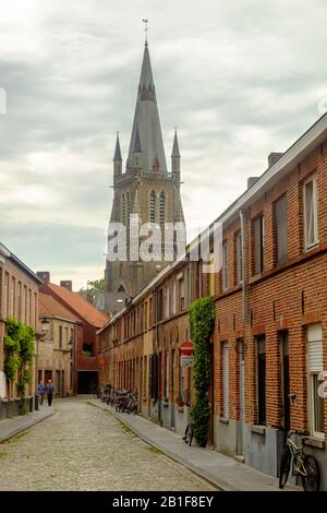 Mit 122 Metern Höhe dominiert die Liebfrauenkirche die Skyline von Brüggen. Im Vordergrund führt eine lange, ruhige Straße zu diesem Wahrzeichen. Stockfoto