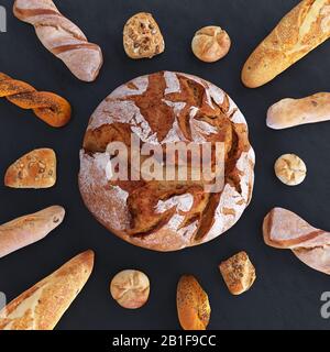 Verschiedene Arten von Brot und Brötchen in der Draufsicht. Brot in Form von Sonne und Strahlen aus Baguettes. Küche oder Backwaren im dunklen Stockfoto