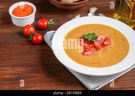 Gemüsesuppe mit Linsen auf Holzgrund. Serviert mit gehackten Kirschtomaten. In der Nähe befinden sich Stücke von Ciabatta. Rohe Groats im Hintergrund. Stockfoto