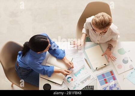 Top-View-Hintergrund von zwei modernen Geschäftsfrauen, die Datentabellen diskutieren, während sie am Tisch sitzen und Platz für Kopien schaffen Stockfoto