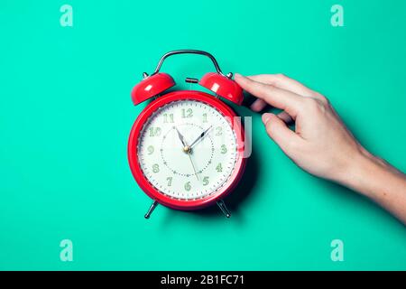 Roter Wecker auf dem Farbhintergrund. Eine Hand von Person, die einen Wecker am Morgen ausschaltet Stockfoto