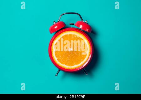 Roter Wecker mit orangefarbenem Obst an der Stelle des Uhrenuhr. Stockfoto