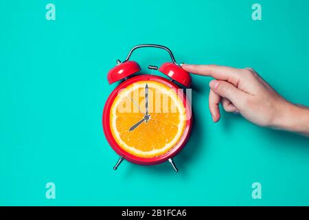 Roter Wecker mit orangefarbenem Obst an der Stelle des Uhrenuhr. Stockfoto