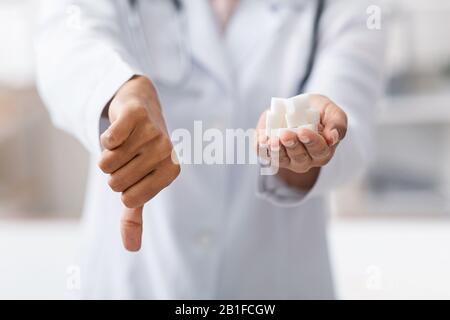 Beschnitten vom Doktor, der raffinierten Zucker hält und Daumen nach oben zeigt Stockfoto