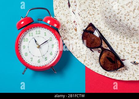 Roter Wecker, Hut und Sonnenbrille auf dem Farbhintergrund. Reise- und Urlaubskonzept Stockfoto