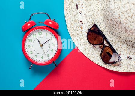 Roter Wecker, Hut und Sonnenbrille auf dem Farbhintergrund. Reise- und Urlaubskonzept Stockfoto