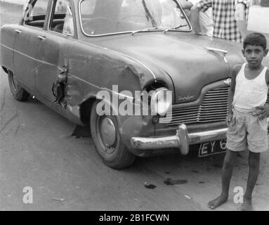 Sri Lanka. 1958. Ein kleiner Junge steht neben einem beschädigten Ford Zephyr Auto. Stockfoto