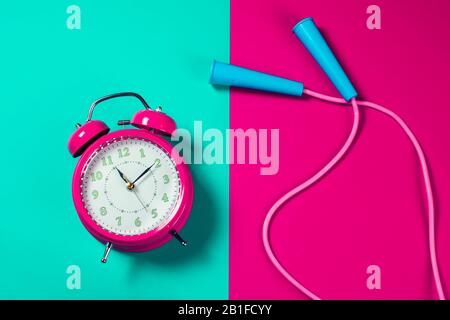 Roter Wecker und Springseil auf dem Farbhintergrund. Fitness- und Gesundheitskonzept Stockfoto