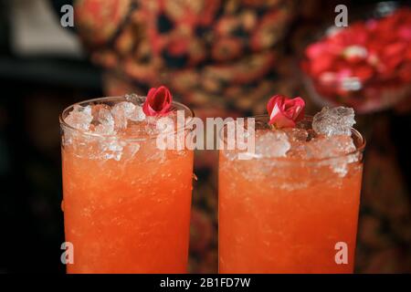 Ein professioneller Barkeeper macht zwei rote Cocktails und schmückt sie mit einer lebenden Blume. Cocktails erhalten Sie an der Bar. Stockfoto