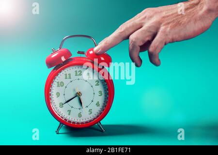 Roter Wecker auf dem Farbhintergrund. Eine Hand von Person, die einen Wecker am Morgen ausschaltet Stockfoto