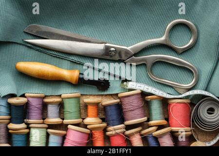 Nähartikel: Retro-Schneiderschere, Maßband, Holzschieber von Fäden, Schneidmesser und grünes Tuch. Draufsicht. Stockfoto