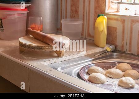 Rollender Stift an einem Schalter einer kleinen voll besetzten Küche neben Chapati, die gerollt wird Stockfoto