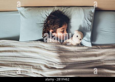 Draufsicht über ein liebenswerliches kleines Mädchen, das im Bett schläft und ihren Teddybären umarmt, glückliche Kindheit und gesundes Ruhekonzept Stockfoto
