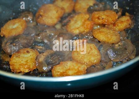 Kochen von Pilzen Zwiebeln und Rösti in einer Bratpfanne mit Ölwürzen und Dampf Stockfoto