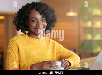 Fröhliches Afro Mädchen, das während der Mittagspause eine Tasse Kaffee genießt Stockfoto