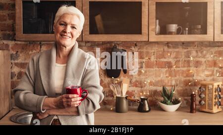 Entspannte Ältere Frau Mit Tasse Kaffee In Der Küche Stockfoto