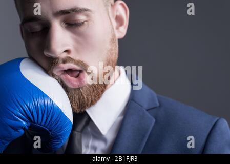 Nahaufnahme eines jungen bärtigen Kerls in einem Business-Anzug, Geschäftsmann, Seitenansicht der Hand eines Gegners in einem Boxhandschuh schlägt. Der Moment von p Stockfoto