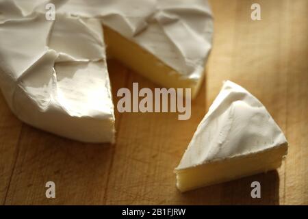 Camembert-Käse mit einem Schichtdreieck auf einem Holztisch. Stockfoto