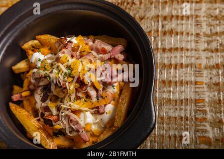 Kasserolle mit rustikalen pommes Frites mit Speck und Käse auf Holzgrund. Isoliertes Bild mit Kopierbereich Stockfoto