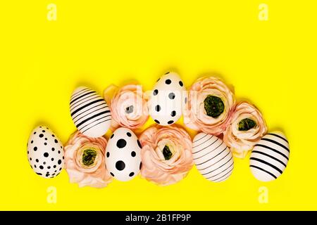 Kreative Grafik von Hand bemalte Eier und ranunculus Blumen auf gelben Hintergrund. Ostern Konzept. Stockfoto