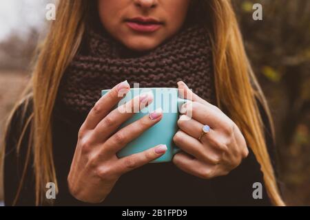 Weibliche Hände mit zartem pinkfarbenem Nageldesign, die den blauen Becher im Freien halten. Schönheit und Wohlbefinden der Frau. Stockfoto