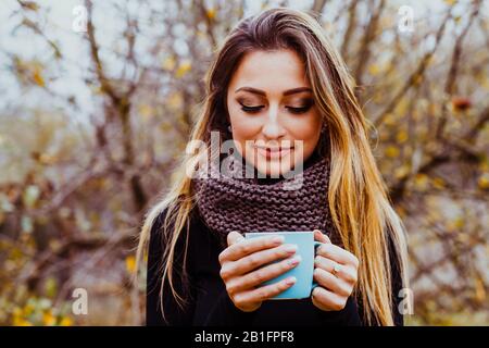 Hübsche Frau mit gepflegten Händen, die draußen eine Tasse heißen Tee hält. Herbsttag. Stockfoto