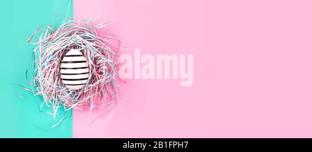 Banner mit grafischem, handbemaltem Linienei in dekorativem Nest auf blauem und pinkfarbenem Pastellgrund. Osterkonzept. Stockfoto