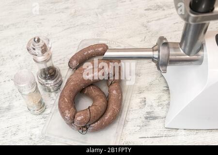 Rohe frische hausgemachte Rinderwürste in natürlicher Schale auf einem Holztisch in der Nähe. Fleischschleifer zum Kochen von Hackfleisch und Gläsern mit Gewürzen. Schnell und nür Stockfoto