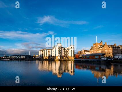 Leith, Edinburgh, Schottland, Großbritannien. Februar 2020. Wetter in Großbritannien: Sonnenschein in der Dämmerung beleuchtet alte und moderne Gebäude am Ufer, die sich im Wasser von Leith widerspiegeln. Das Malmaison Hotel (ehemalige Seemannsmission) und ein moderner Apartmentblock namens Queen's Quay Stockfoto