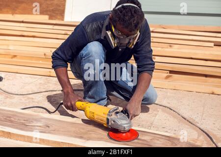 Ein Handwerker in Maske poliert Holzplanke im Freien. Stockfoto