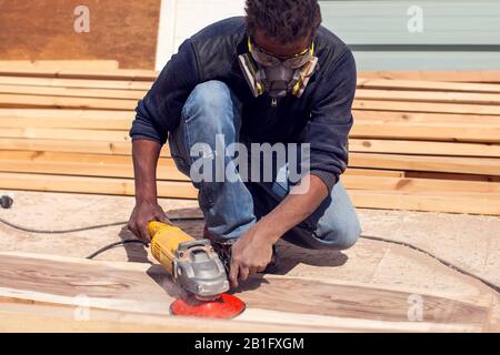 Ein Handwerker in Maske poliert Holzplanke im Freien. Stockfoto