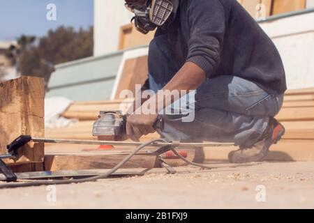 Ein Handwerker in Maske poliert Holzplanke im Freien. Stockfoto