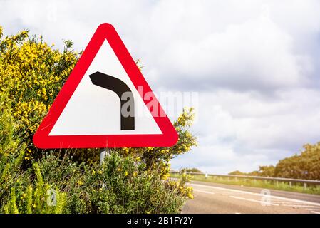 Gefährliche Kurve vor dem Warnschild auf einer Küstenstraße an einem sonnigen Frühlingstag Stockfoto