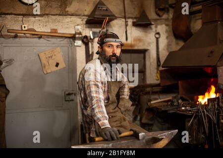 Das Porträt des bärtigen Schmieds, der sich auf die Arbeit in seiner Werkstatt vorbereitet. Kleine Unternehmen. Stockfoto