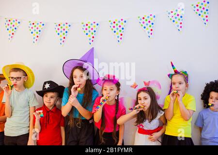 Fröhliche freudige Kinder feiern Geburtstag und tragen lustige Partymützen. Niedliche Kinder bläschen Pfeifen Stockfoto
