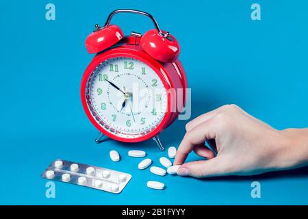 Roter Wecker, Pillen auf Farbhintergrund. Hand der Frau, die Pille nimmt. Konzept für das Gesundheitswesen und die Medizin Stockfoto