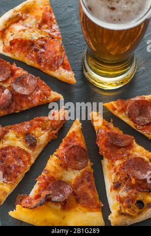 Köstliche frisch gekochte Scheiben von Pfefferoni Pizza auf Schiefer und Glas Bier Stockfoto